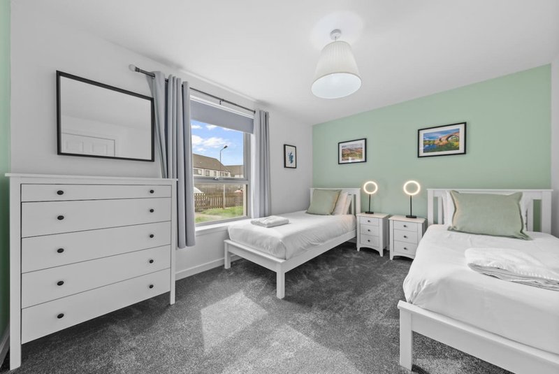 Bright bedroom with two single beds, white furniture, green walls and garden view