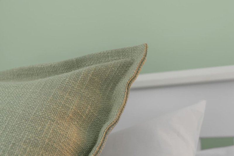 Close-up of green linen cushion with tan piping detail on bed