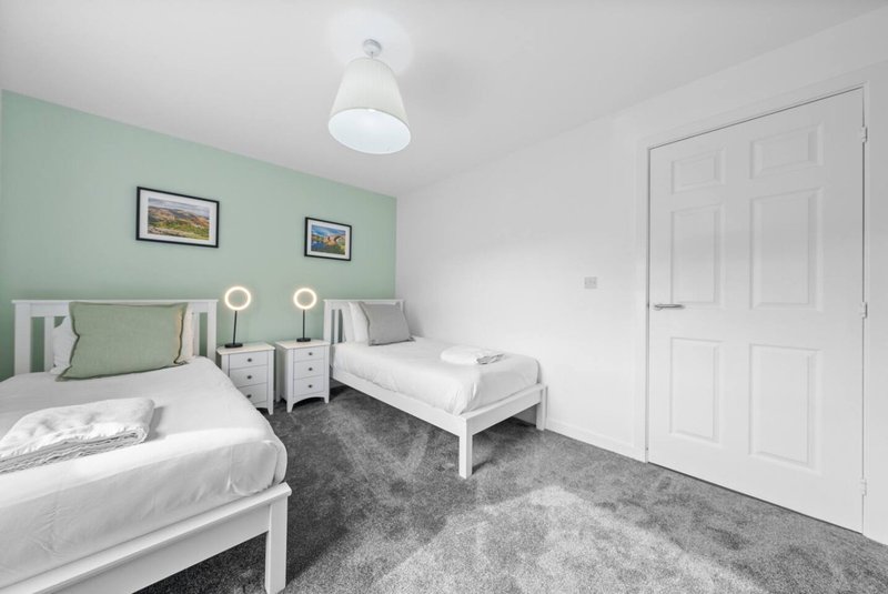 Twin bedroom with mint green accent wall, white beds, grey carpet and ceiling light