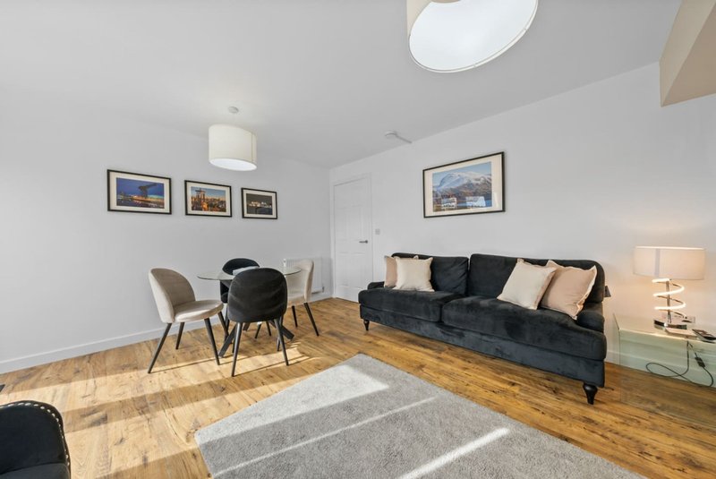 Modern living room with dark sofa, dining chairs, wooden floors and framed wall art