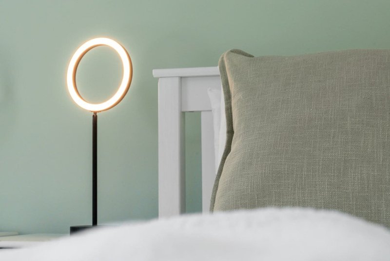 Bedroom with upholstered headboard, white bedding, ring lamp, and pale green walls