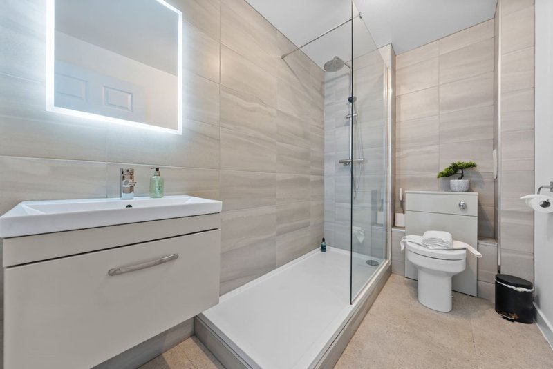 Modern bathroom with vanity, illuminated mirror, walk-in shower and toilet