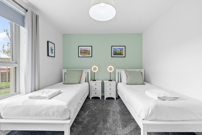 Twin bedroom with white beds, green accent wall, framed artwork and ceiling light