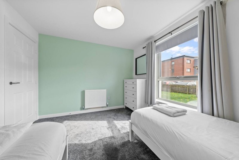 Twin bedroom with mint green accent wall, two beds, window overlooking garden and building exterior