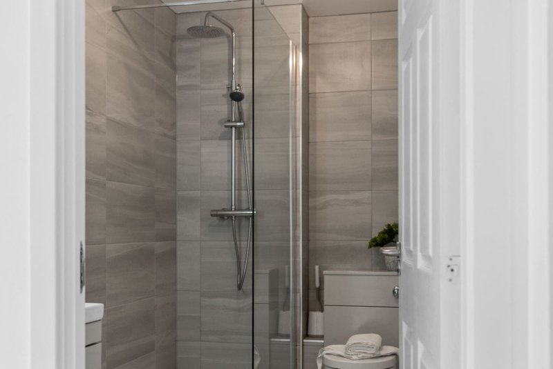 Modern bathroom with walk-in shower, glass enclosure, gray tile walls and white fixtures