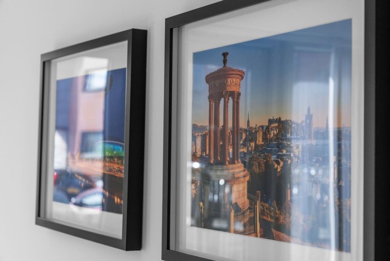 Two framed architectural prints on white wall, left frame shows blurred interior scene, right frame shows cityscape with tower