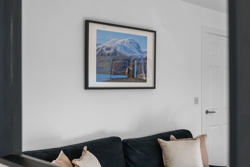 Living room with black sofa, beige cushions, framed mountain landscape artwork on white wall