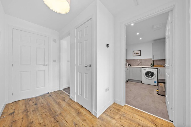 Bright hallway with wooden flooring, white doors, and view into kitchen with washing machine