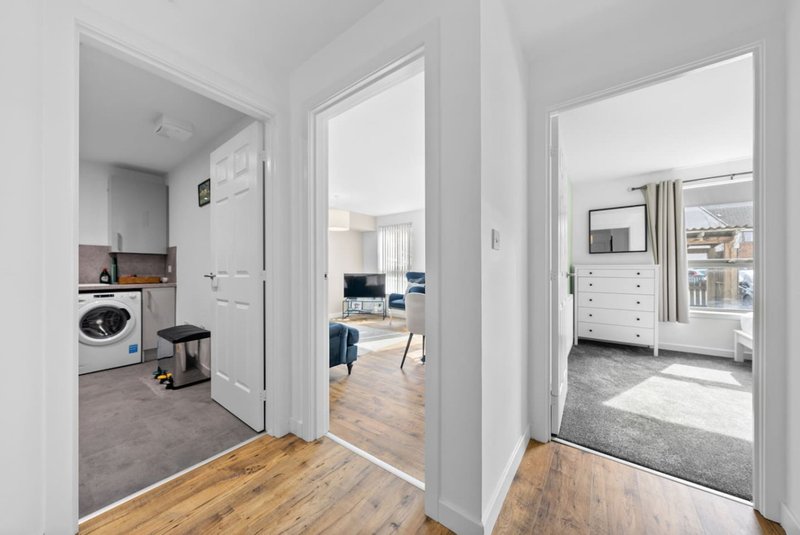 Hallway with wooden flooring opening to laundry room, bedroom, and living spaces
