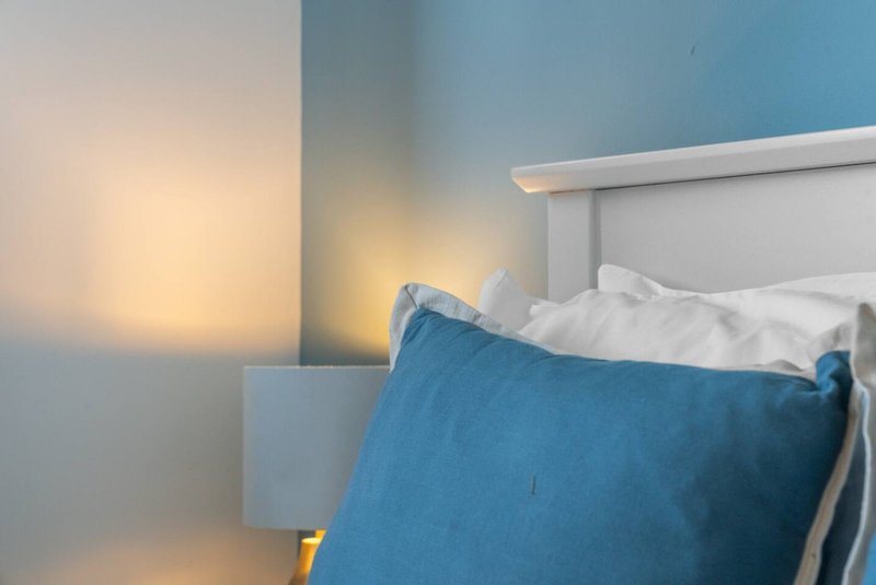 Bedroom with blue cushion, white bedding, and warm ambient lighting