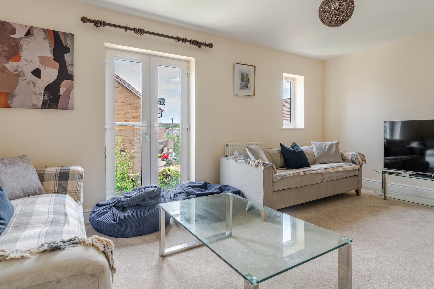 Spacious living room with sofa, armchair, glass coffee table and patio doors to garden