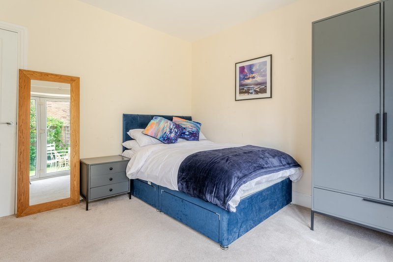 Bright bedroom with blue upholstered bed, grey bedside table, wooden mirror door and grey wardrobe