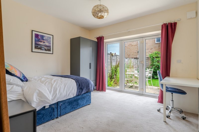 Bright bedroom with double bed, desk, wardrobe and glass doors opening to garden
