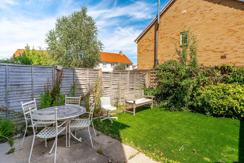 Garden with circular table, chairs, bench, fencing, and brick house exterior