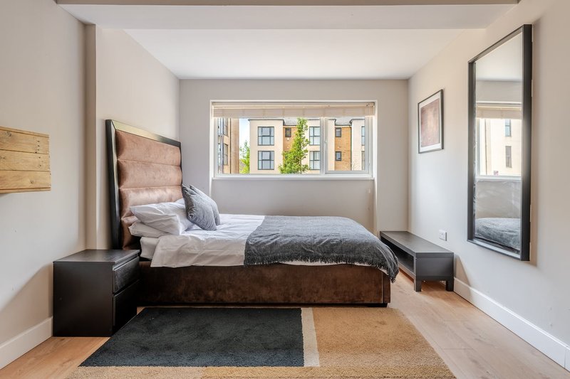 Modern bedroom with double bed, wooden headboard, bedside tables and large window overlooking street