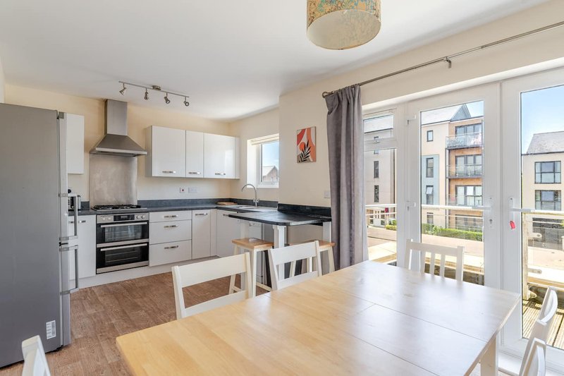 Modern kitchen with white cabinetry, black countertops, dining table and balcony doors overlooking residential building