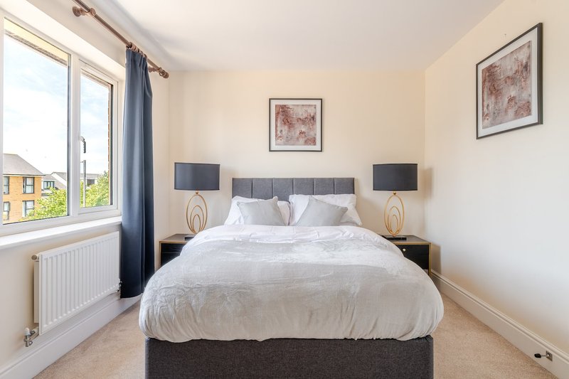 Bright bedroom with double bed, two bedside lamps, window with blue curtains overlooking street