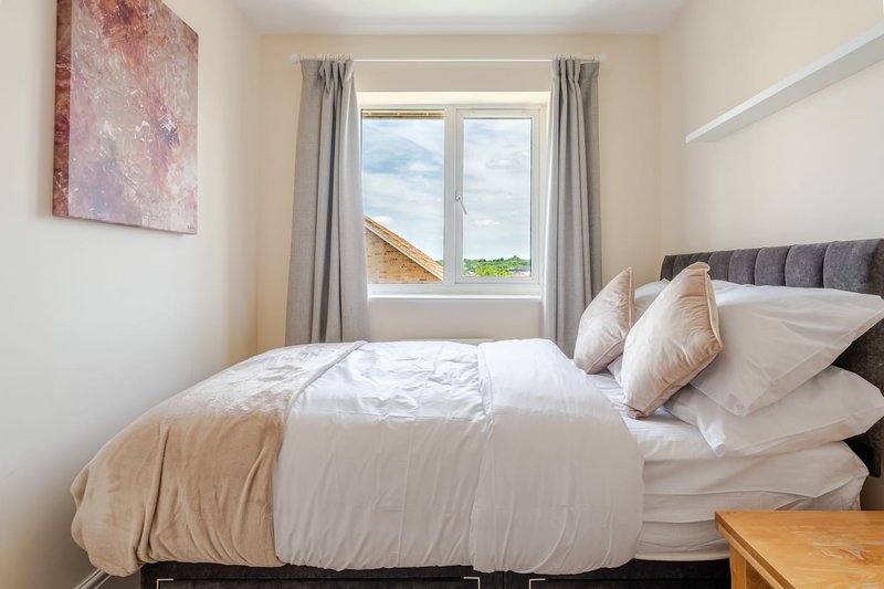 Modern bedroom with double bed, grey headboard, cushions, and window view of countryside