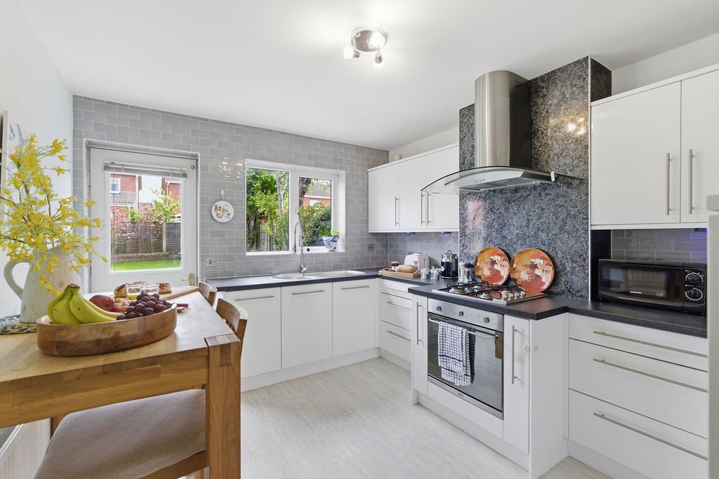 Modern kitchen with white cabinetry, stainless steel appliances, grey tile backsplash and wooden dining table