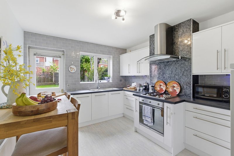 Modern kitchen with white cabinetry, stainless steel appliances, grey tile backsplash and wooden dining table