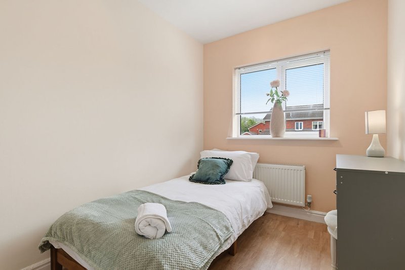 Bedroom with single bed, green bedding, wooden floor and window overlooking street