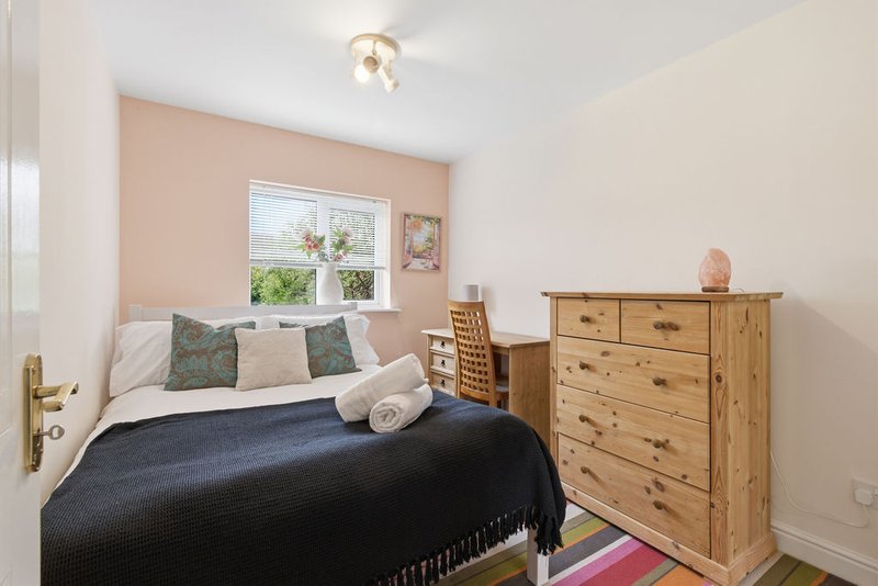 Bedroom with double bed, wooden dresser, peach accent wall and window with garden view