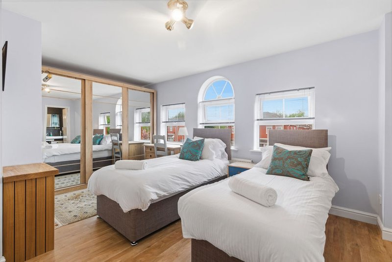 Bright bedroom with two single beds, wooden flooring, large windows with city views, and mirrored doors