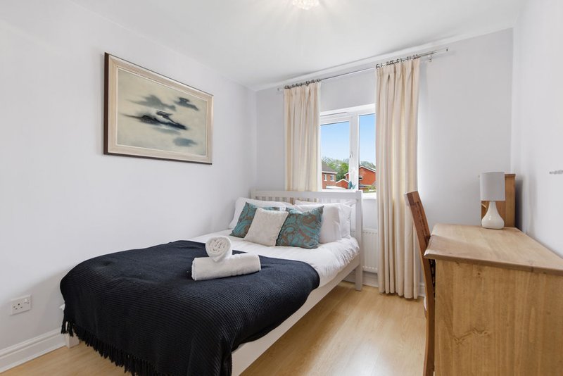Bright bedroom with single bed, black throw, wooden desk, framed artwork and cream curtains