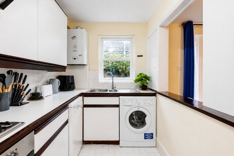 Modern kitchen with white cabinetry, dark countertops, washing machine, window with garden view