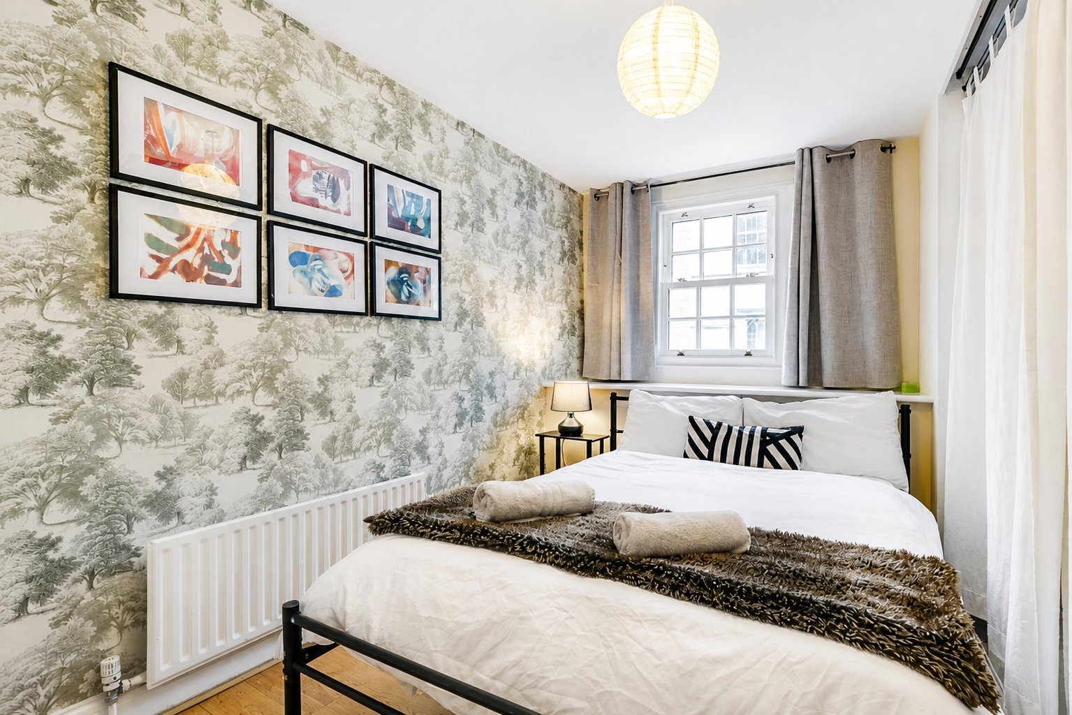 Modern bedroom with two beds, framed wall art, patterned wallpaper and pendant light