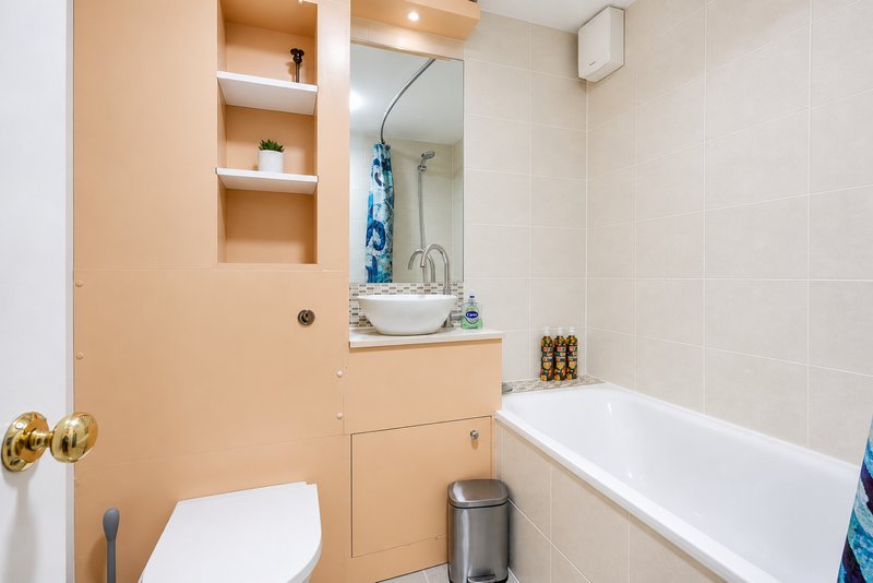 Modern bathroom with peach vanity, round sink, bathtub, toilet and mirrored medicine cabinet