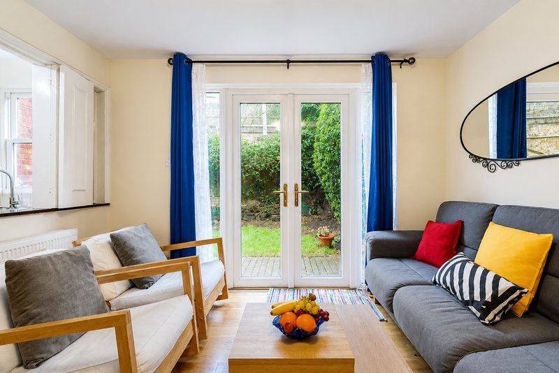 Bright living room with gray sofa, wooden chairs, blue curtains and garden doors