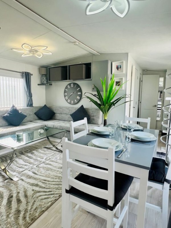 Open-plan living and dining area with white furniture, grey sofa, dining table and kitchen visible