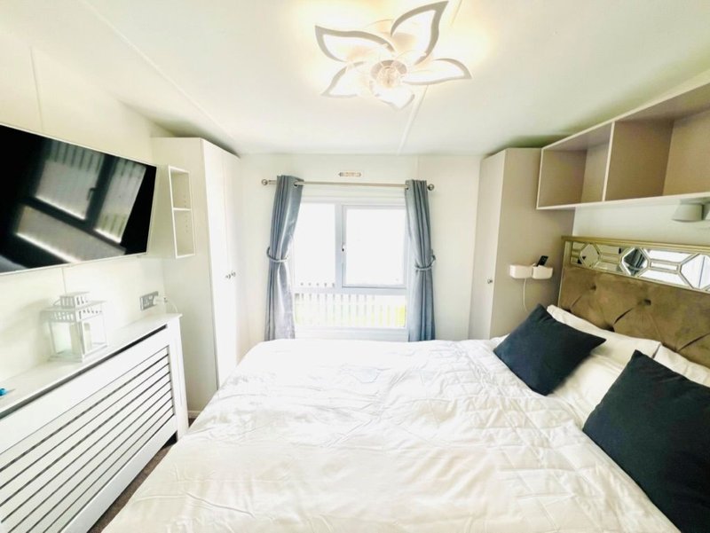 Modern bedroom with double bed, black pillows, wall-mounted TV, and balcony doors