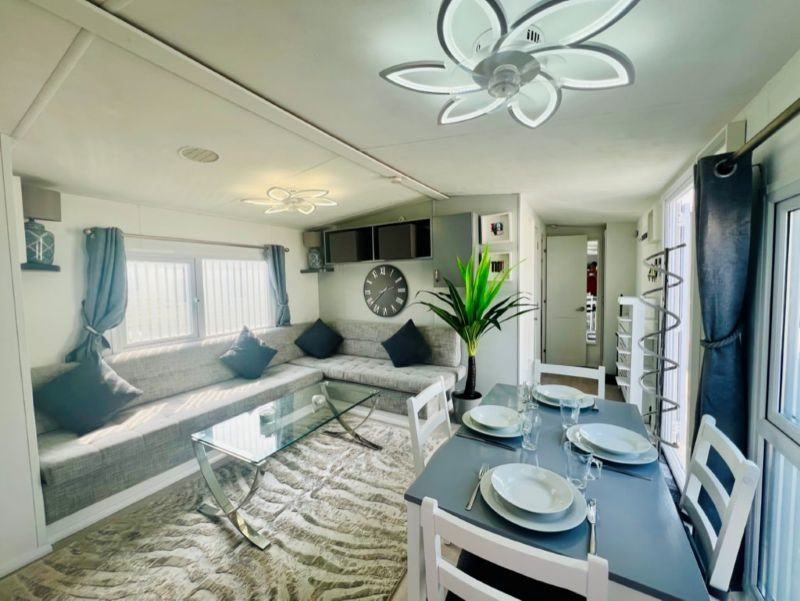 Open-plan living area with window seat, dining table, modern ceiling fan and green plant decor