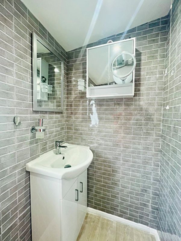 Modern bathroom with brick tile walls, white pedestal sink, mirror cabinet and shower area