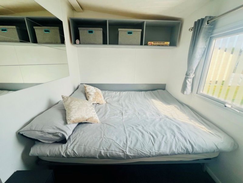 Compact bedroom with gray double bed, patterned pillow, wall storage, and window with curtains