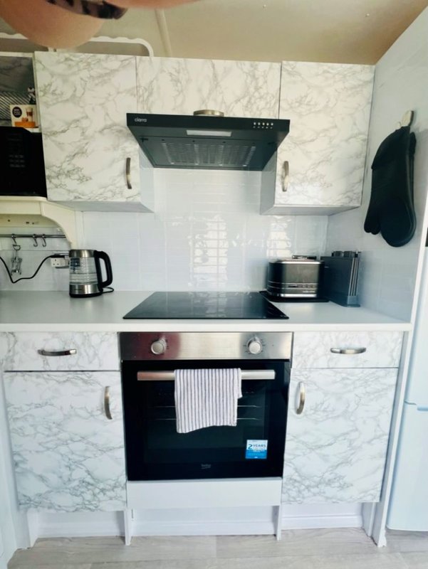 Modern kitchen with marble backsplash, black range hood, built-in oven and white cabinetry