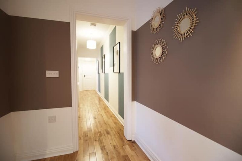 Hallway with two-tone walls, wooden flooring, and decorative sunburst mirrors