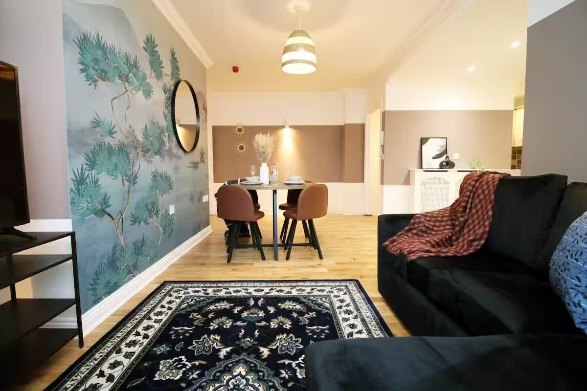 Open-plan living area with black sofa, dining table, kitchen, and botanical wall art