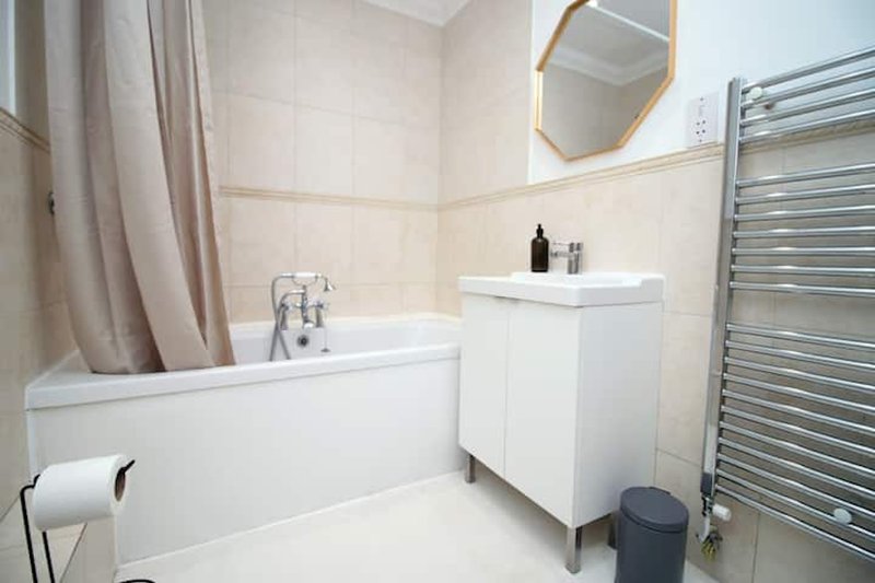 Modern bathroom with white bathtub, vanity sink, heated towel rail and mirror