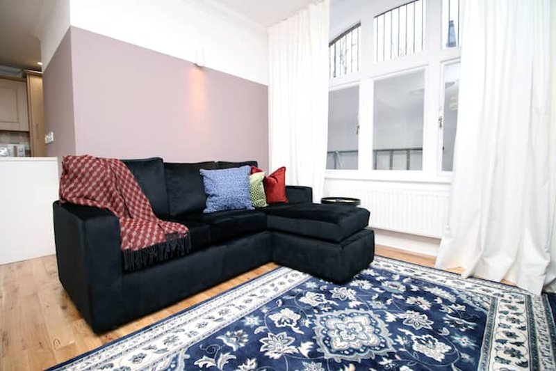 Living room with black sectional sofa, patterned rug, and large windows with white curtains