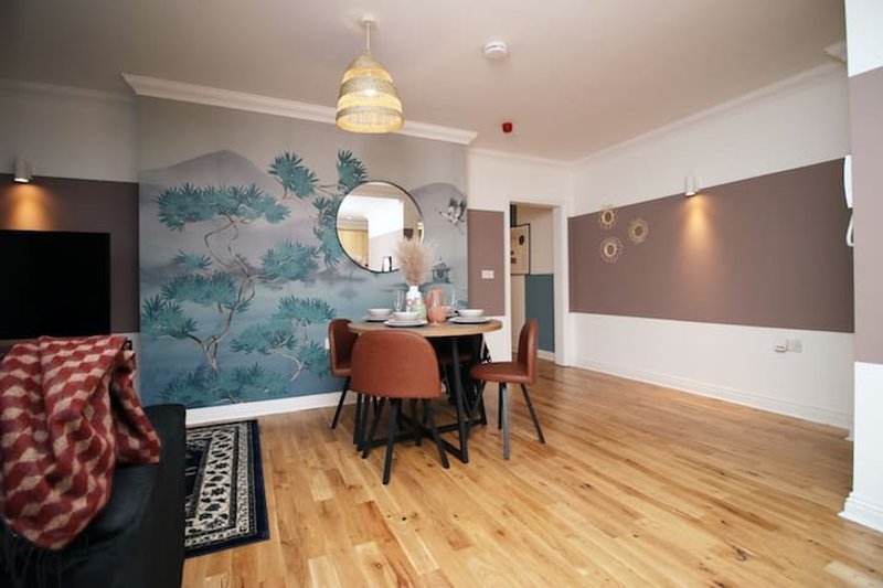 Open-plan living and dining area with wooden floors, teal wallpaper, and pendant lighting