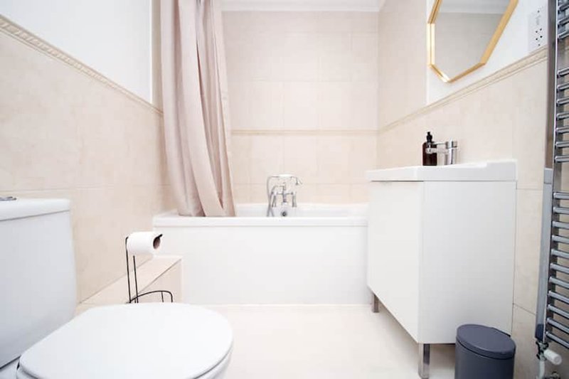 Clean modern bathroom with white toilet, bathtub, sink vanity and mirror