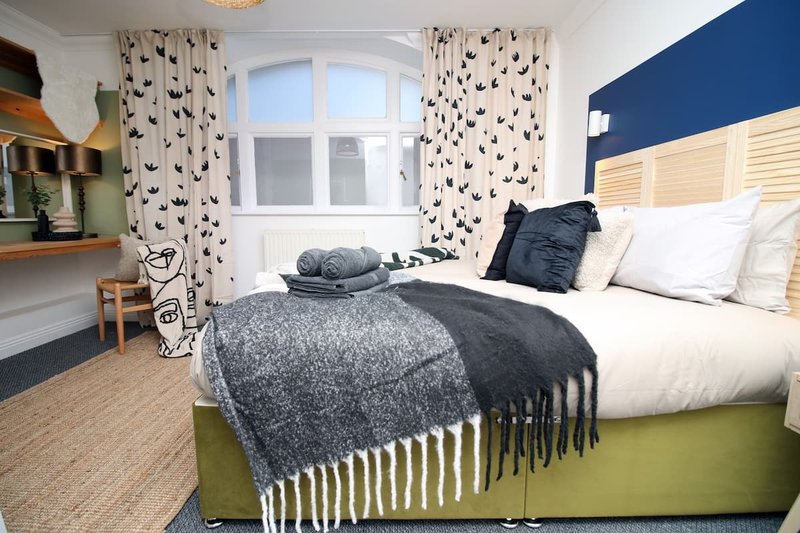Bedroom with double bed, navy accent wall, patterned curtains, and desk area by window