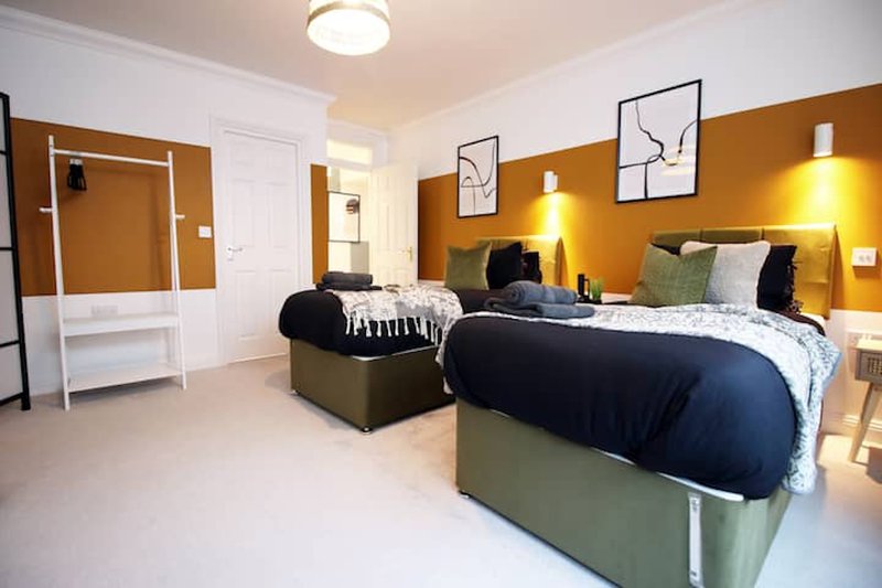 Bright twin bedroom with two beds, mustard accent wall, modern artwork and en-suite door