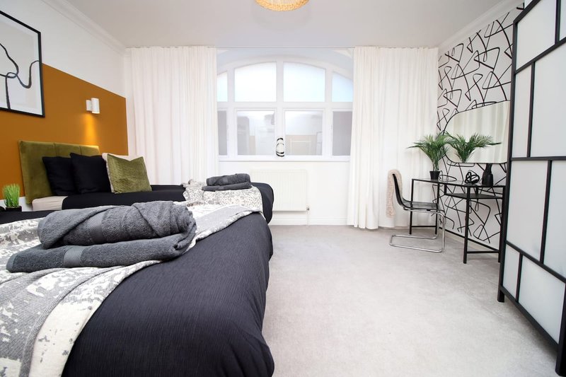 Bright bedroom with double bed, mustard accent wall, large windows and potted plant
