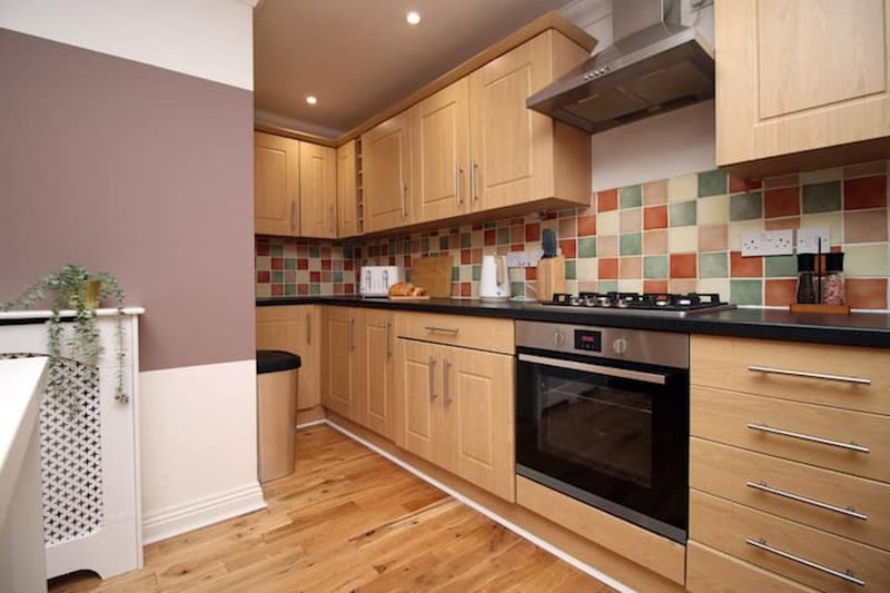 Modern kitchen with wooden cabinets, colorful tile backsplash, stainless steel appliances and wooden flooring
