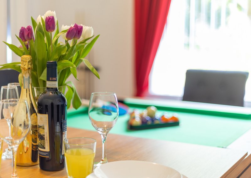 Dining table with flowers, wine bottles, glasses, and billiard balls in background