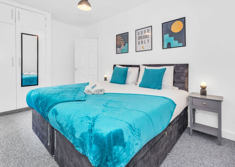 Modern bedroom with turquoise bedding, teal cushions, wall art, and grey bedside furniture